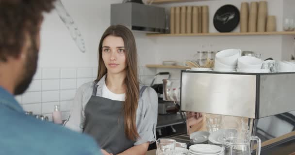 Barista femenina hablando con un cliente que recibe un pedido para preparar un café recién hecho. Movimiento lento . — Vídeos de Stock