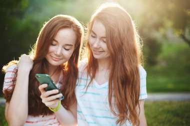 Genç kadın Smartphone vasıl arıyor. İki kız kardeş bir cep telefonu sosyal medya yoluyla kaydırma Kızıl. Kablosuz iletişim geleceğimiz var. Yaşam tarzı kavramı.