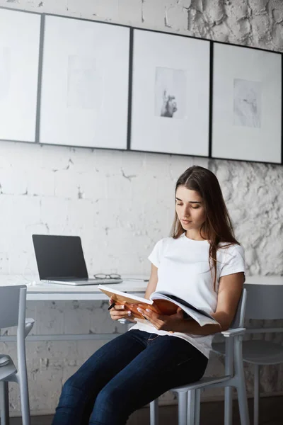 Wanita muda membaca majalah santai setelah berjam-jam bekerja di komputer laptopnya . — Stok Foto