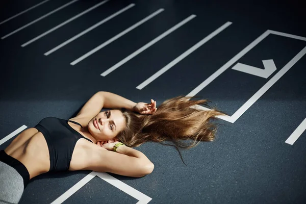 Retrato de una mujer ídolo de fitness adulta tumbada en el suelo del gimnasio mirando a la cámara sonriendo. Perfecto equilibrio cuerpo y alma . — Foto de Stock