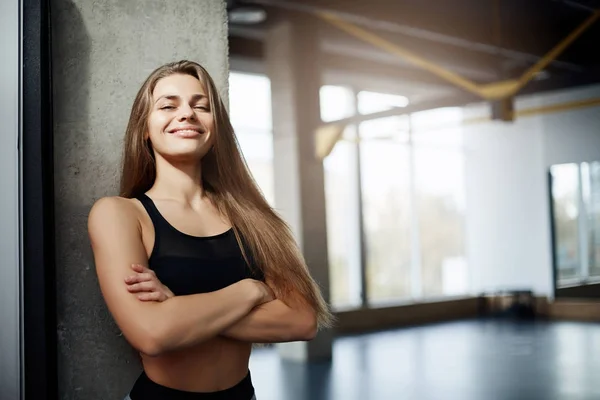 Porträt einer erwachsenen Fitnesstrainerin, die in die Kamera blickt, mit leerem Fitnessstudio im Hintergrund. Fittes Körperkonzept. — Stockfoto