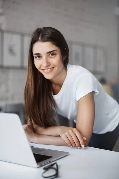 Portrait of beautiful caucasian woman using laptop computer standing in open space coworking centre looking for new job looking at camera smiling.