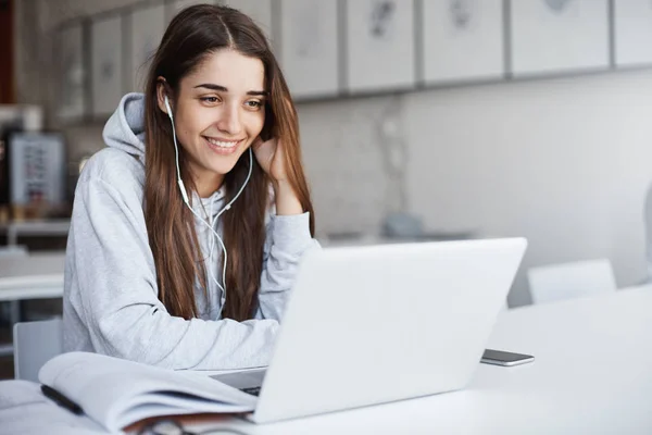 Joven chica perfecta usando computadora portátil viendo videos en línea usando auriculares blancos con cable sonriendo —  Fotos de Stock