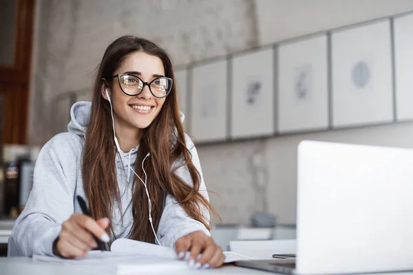 Giovane insegnante di sesso femminile con gli occhiali che si prepara per la sua classe ascoltando musica ottimista utilizzando computer portatile sorridente . — Foto Stock