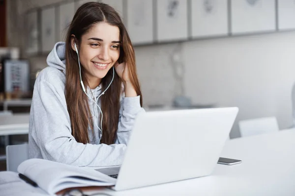 Young perfect girl using laptop computer watching online videos using wired white earphones smiling laughing Stock Picture