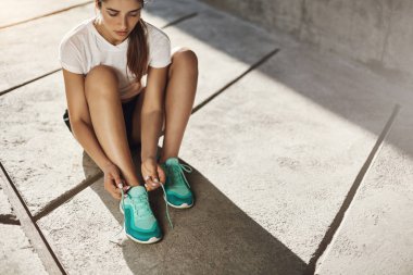 Uzun koşuya hazır Başlarken spor ayakkabılarını bağlama beton zemin üzerinde oturan genç kadın atlet