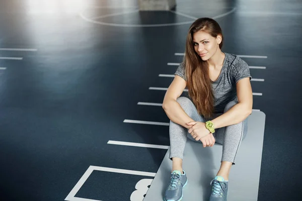 Portirait de jovem atleta feminina de cabelos compridos fazendo uma pausa do treino duro sentado no tapete olhando para a câmera sorrindo . — Fotografia de Stock