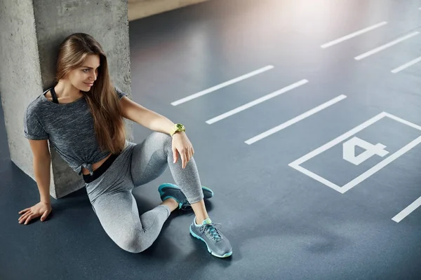 Body fitness woman coach sitting on gym floor planning her new training session. Strong biceps and triceps.