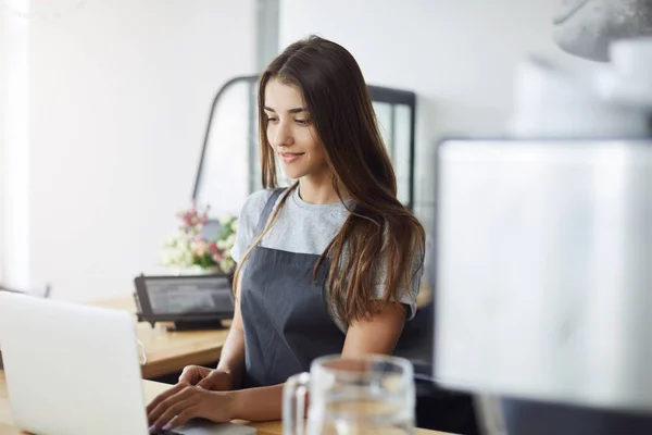 Retrato de una joven dueña de una cafetería usando un portátil esperando a su primer cliente temprano en la mañana. Mujer dirigiendo su negocio . — Foto de Stock