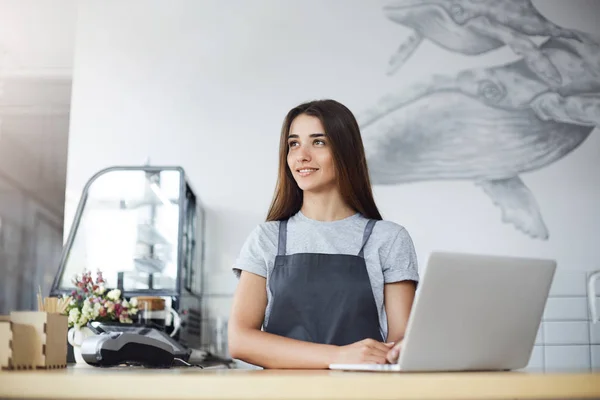 Potret barista perempuan beristirahat sejenak dari pekerjaannya di kafe yang sibuk menikmati sinar matahari dengan menggunakan laptop . — Stok Foto