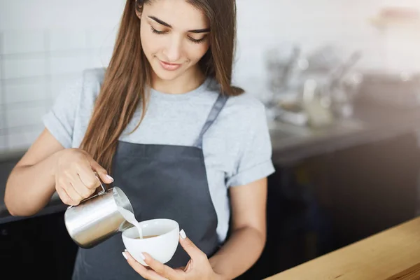 สาวบาริสต้ามืออาชีพเทโฟมนมลงในกาแฟเพื่อสร้างศิลปะลาเต้โดยใช้เหยือกและถ้วย . — ภาพถ่ายสต็อก
