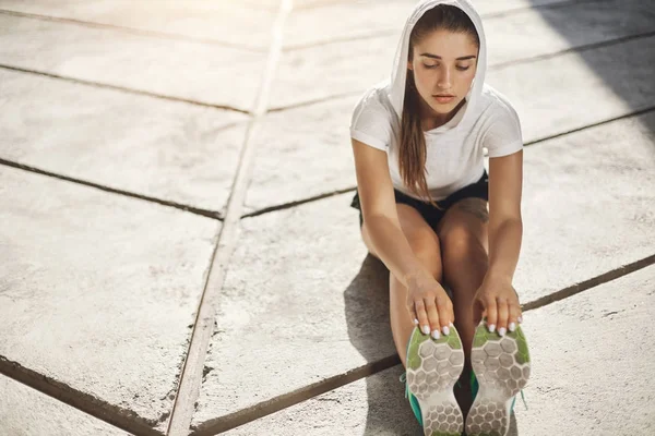 Junge Läuferin, die sich dehnt, bevor sie einen Lauf ihres Lebens in urbaner Umgebung beginnt. Sport macht uns stärker. — Stockfoto