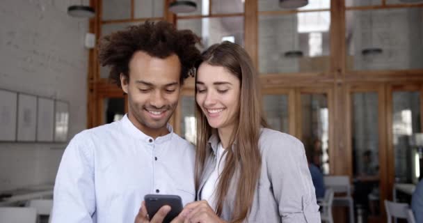 Młody mieszane rasy para studentów lub coworking dyskusji na temat nowego projektu aplikacji. Mężczyzna kobieta wyświetlone inteligentny telefon i śmiejąc się. — Wideo stockowe