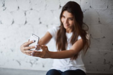 Bulanık eller üzerinde odaklanılan selfie yaparken smartphone vasıl gülümseyen çekici Avrupa esmer kadın portresi. Moda kız onun aboneleri ile konuşmak için canlı akışı başlar