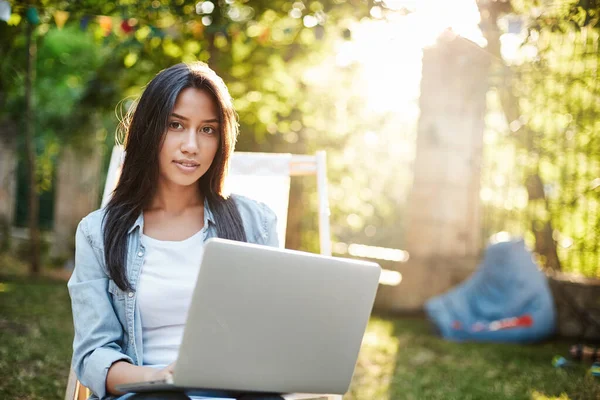 Online education, freelance and nature concept. Beautiful woman in denim jacket, t-shirt relaxing on picnic chair in green cozy park, hold laptop and gaze camera, working remote, study outdoors