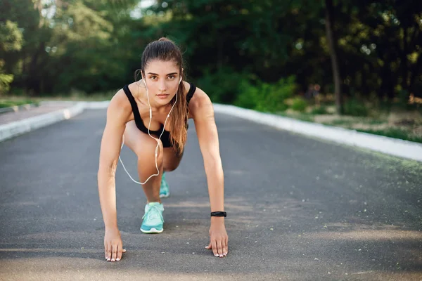 Koncept sportu, fitness a městského životního stylu. Motivovaný dobře vypadající žena vést aktivní život, dělat ranní běh, sprinter stát nízký start na betonové silnici, podívejte se kamera odhodlaný, jogging trénink — Stock fotografie