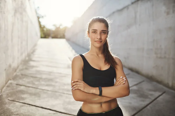 Can you beat her running record. Motivated and confident sportswoman in black sportsbra and shorts, wear fitness tracker, cross arms self-assured look camera, jogging in morning under summer sun — Stock Photo, Image