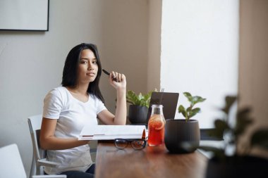 E-öğrenme, kadın serbest ve dijital göçebe konsepti. Güzel akıllı öğrenci pencerenin yanında dizüstü bilgisayar kullanarak oturur, kalemle gülümseyen kamera olarak oynar, web sitesinden notlar alır, ders çalışır.