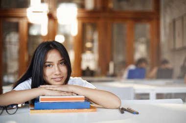 Eğitim, dijital göçebe ve genç yaşam tarzı konsepti. Kafede okuyan güzel bir kız öğrenci, kitap yığınlarına ve gülümseyen kameralara uzanır, kalkış gözlükleri ödevlerine ara verir, dışarıda öğrenim görür.