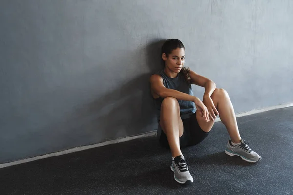 측면 샷멋지게 보이고, 활동적 인 운동 여성의 동기 부여 운동 후 휴식을 취하고, 체육관 벽에 기대고, 앉아서, 건강 강사는 기능적 인 훈련을 시작 한다 — 스톡 사진