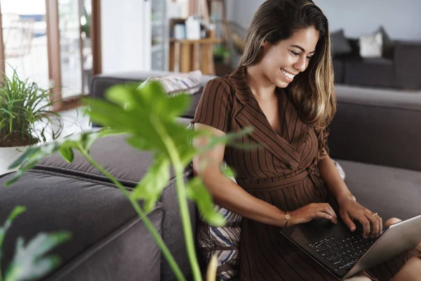 Concepto nómada financiero, empresarial y digital. Mujer brasileña atractiva feliz usando el ordenador portátil, sonriendo como pantalla del dispositivo del aspecto, sala de estar, sofá de oficina cerca de plantas y balcón, trabajando a distancia — Foto de Stock