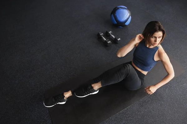 Motivated attractive slim and masculine female athlete, sportswoman lifting body up as crunching, fitness training to get stronger as workout on abdominal abs, look aside, lift one leg, train in gym — Stock Photo, Image