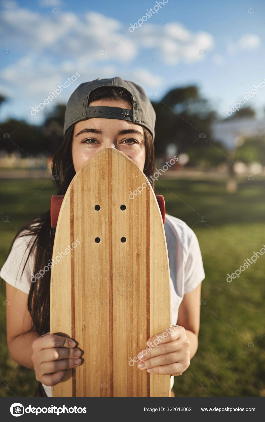 Vertical shot carefree teenage hipster girl in grey snapback, cover face with wooden penny board, eyes smiling and gazing camera, teenager enjoying summertime vacation riding skaterboard park Stock Photo by ©ringsaroundme