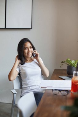 Vertical shot beautiful cheerful young woman take-off glasses, take break from studying in cafe, lean on chair smiling talking on smartphone, female freelancer working remote sit near window relaxed
