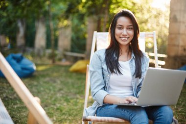 Freelancing, vanlife and digital nomad concept. Alluring young successful female entrepreneur work on fresh air enjoy nature, sit in park on picnic chair, hold laptop on laps smiling camera pleased