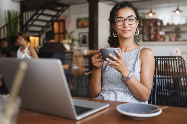 Relaksasi, masyarakat perkotaan dan konsep pendidikan. Pekerja lepas wanita muda yang menarik, siswa yang sedang istirahat dari pekerjaan, memesan kopi, memegang cangkir dan menikmati cappuccino, tersenyum senang, menggunakan laptop — Stok Foto