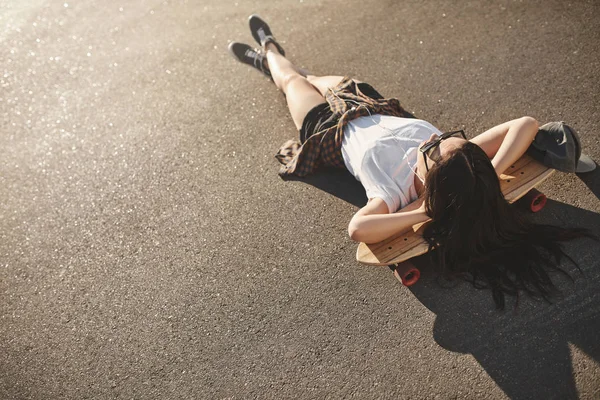 Skater-Lifestyle, urbane Freizeit und Jugendkonzept. Hipster-Teenager genießen Sommerferien, liegen auf Betonstraße des Skateparks auf Penny-Board und hören Musik in kabelgebundenen Kopfhörern — Stockfoto