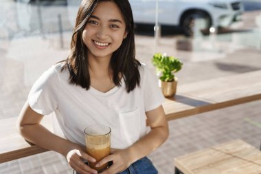 Modern şehir yaşam tarzı, gençlik ve insan konsepti. Yakın plan çekici Asyalı kadın gülümsüyor ve kameraya mutlu bir şekilde bakıyor işten sonra kafede dinlenirken arkadaşlarıyla konuşuyor, kahve içiyor.