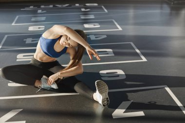 Dayanıklılık, sabır ve egzersiz konsepti. Kararlı, odaklanmış, spor salonunda iyi görünümlü atletik kadın, sporcu kadın ısınmak için vücudunu esnetiyor, yerde oturuyor, vücudunu büküyor ve kollarını kaldırıyor.