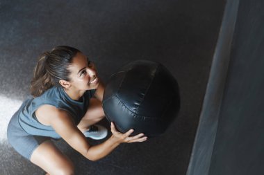 Üst açı şutu, motive olmuş mutlu ve kararlı genç lezbiyen kadın, fitness eğitmeni çömelme egzersizi yaparken topu kaldır, kas kazan, spor salonunda kaslarını çalıştır, mutlu gülümse.
