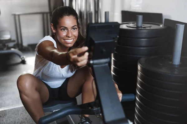 Schön aussehende hispanische junge Aktivkleidung in Aktivkleidung, auf dem Bildschirm des Fitnessgeräts sitzen, um Beinpresse zu programmieren, Workout während des Functional Trainings, motiviert und glücklich lächelnd — Stockfoto