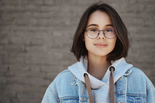 Close-up retrato despreocupado otimista jovem estudante de cabelos curtos em óculos ansiosos para oportunidades de vida, sorrindo câmera de aparência sonhadora, de pé perto da parede de tijolo ao ar livre — Fotografia de Stock