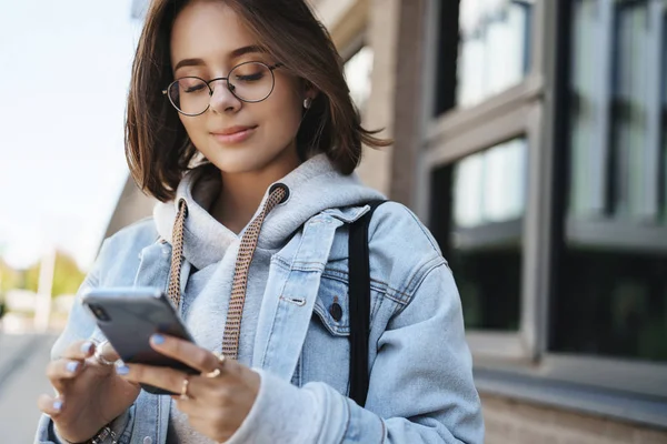 Close-up portrait tender romantic girlfriend send cheerful message, heart emoji friend, holding mobile phone and smiling at display, texting with friend, communicating while standing on street — Stock Photo, Image