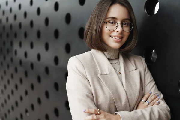 Career opportunities, women and education concept. Close-up portrait of stylish smiling woman looking at camera with pleased confident look, cross hands chest, lean office wall — Stock Photo, Image