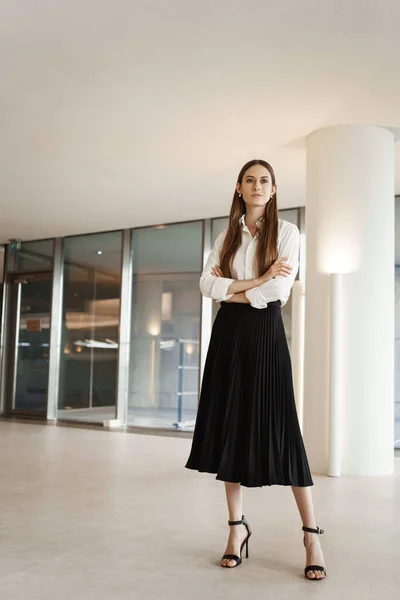 Vertical shot of proud and confident, successful businesswoman in company office, standing assured with crossed hands, looking pleased on distanse as thinking new deals and productive projects Stock Picture