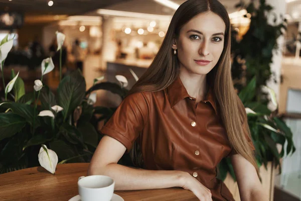 Successful young female restaurant owner, businesswoman leaning hand on table, looking at camera with pleased, happy smile, drinking cup coffee in fancy cafe, enjoying relaxing weekend — Stock Photo, Image