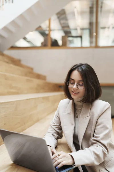 Verticaal portret van professionele, succesvolle jonge kortharige vrouw in beige jasje, typt boodschap naar cliënt met laptop, werkt aan remote, online project, studeert of freelancet — Stockfoto