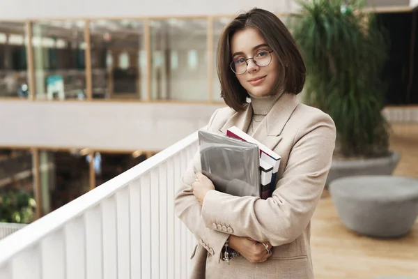 Pendidikan, bisnis dan konsep wanita. Potret tutor perempuan muda yang menarik dan elegan, guru muda atau murid membawa buku-buku pelajaran dan laptop, yang berdiri di aula sambil tersenyum — Stok Foto