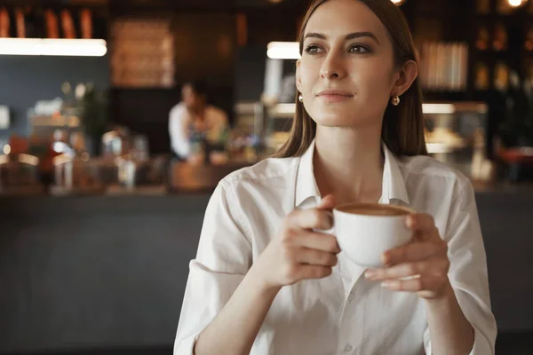 Jovencita relajada satisfecha, mujer de negocios tomando café en la cafetería, mirando por la ventana disfrutando de un agradable ambiente acogedor, teniendo descanso de oficina, sonriendo pensativamente, ocio y concepto de negocios —  Fotos de Stock