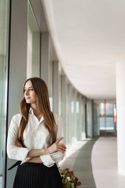 Business and women concept. Elegant successful female entrepreneur looking out window as standing office corridor, contemplating view satisfied with good business deal, meeting went well Stock Photo