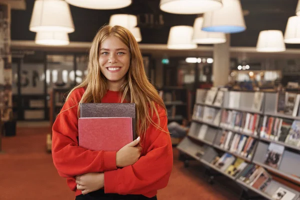 การเรียนรู้ มหาวิทยาลัย และแนวคิดทักษะใหม่ๆ ยิ้มอย่างมีความสุข สาวหัวอ่านถือหนังสือ ยืนอยู่ในห้องสมุดหรือร้านหนังสือ เตรียมการบ้าน ทําวิจัยสําหรับโครงการวิทยาลัย — ภาพถ่ายสต็อก
