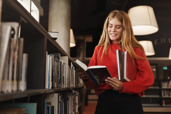 Pendidikan, pembelajaran dan konsep pertumbuhan pribadi. Gadis berambut merah yang menarik, siswa yang berdiri di perpustakaan dekat rak, membaca buku dan tersenyum, belajar, memilih novel di toko buku, menyiapkan PR — Stok Foto