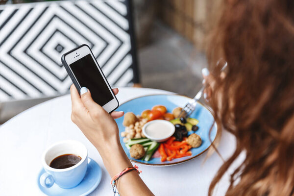 Management, dining-out and people concept. Side shoulder view of woman hand using mobile phone, checking messages while eating at restaurant or cafe, contact client while at lunch Royalty Free Stock Photos