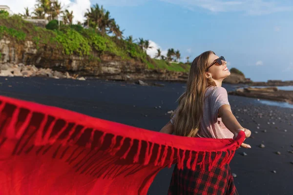 Happiness, summer lifestyle and recreation concept. Happy, carefree young woman enjoying sunbathing, warm sun on sandy black beach, volcanic sand, looking at ocean, pareo flown by wind — Stock Photo, Image