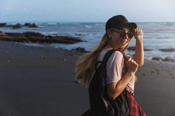 Viajante mochileiro feliz, hipster menina viajar ao redor do mundo com mochila, voltar para sorrir câmera, explorar a Ásia com namorado, desfrutar de caminhar praia deserta com areia preta, sorrindo — Fotografia de Stock