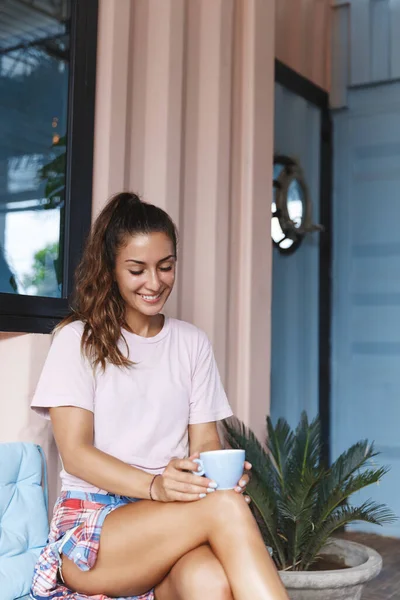Stay safe, comfort and relaxation concept. Vertical shot of romantic, pretty woman smile at cup of tea, feel comfort, fill leisure with hapy small moment during lockdown at home on self-quarantine